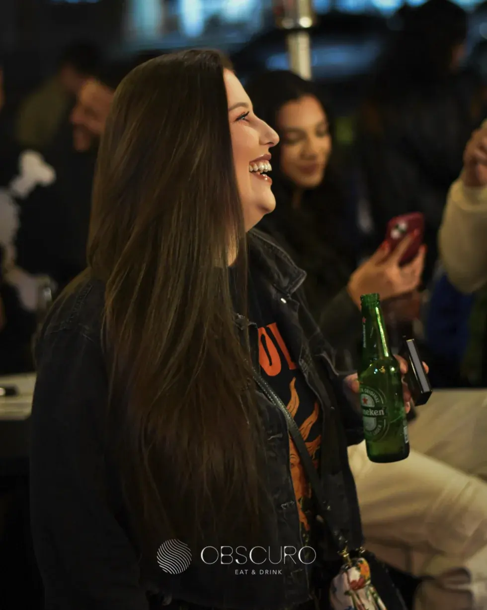 Cliente rindo com uma cerveja na mão durante a noite no Obscuro